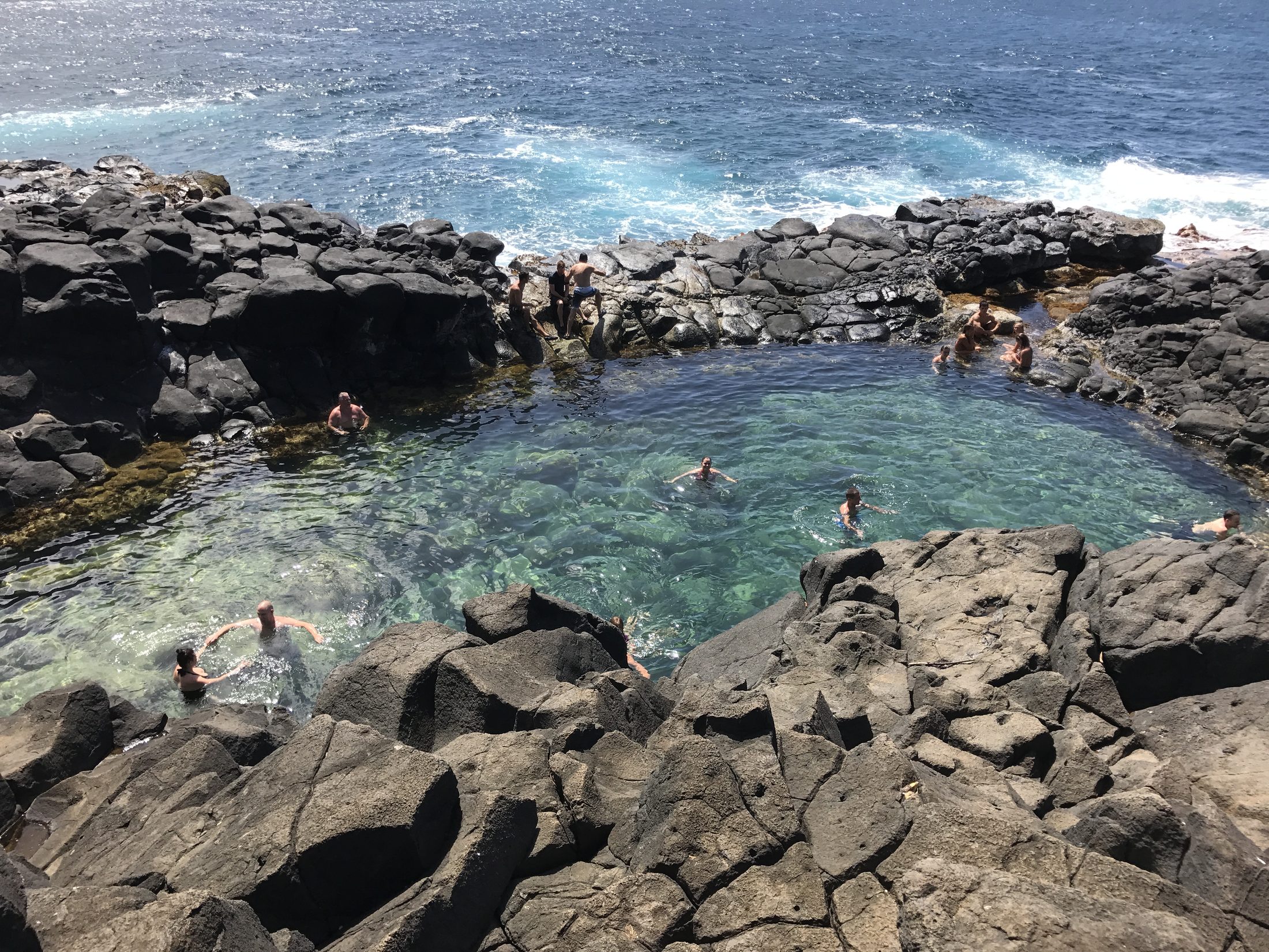 Swimmers in a clear rock pool carved into black lava on Kauai's north shore. Ulana Rey PharmD